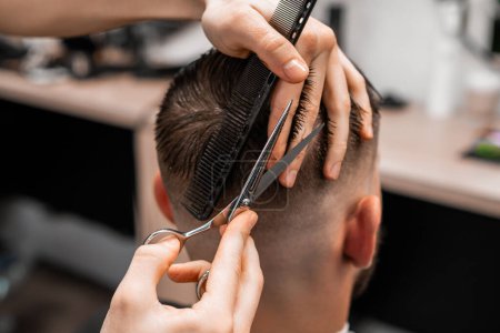 Barber uses scissors and a comb to cut the hair on the back of a mans head in a barbershop.