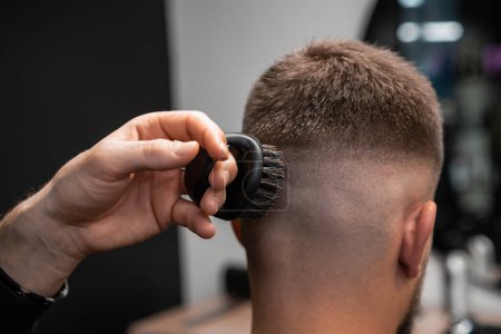 Hairstylist removes hair behind client ear and occiput with shaver in barbershop closeup. Barber uses modern machine for stylish haircut in salon