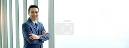 Photo for Smart and good looking Asian businessman looking at the camera and crossed arms. Photograph with copyspace. - Royalty Free Image