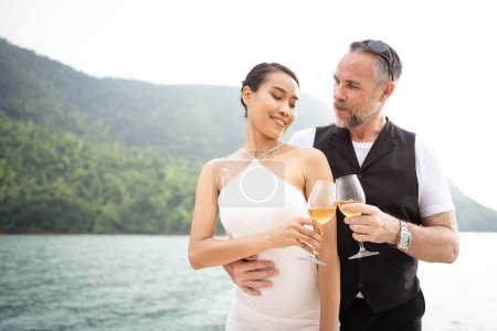 Téléchargez les photos : Heureux couple blanc asiatique et caucasien célébrant ensemble leur anniversaire de mariage sur le yacht. Couple adulte naviguant sur un yacht et buvant un champagne ensemble lors d'un voyage de lune de miel. - en image libre de droit