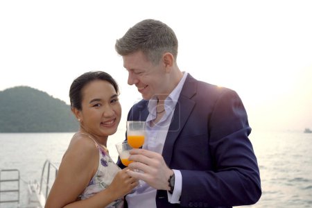 Téléchargez les photos : Heureux couple blanc asiatique et caucasien célébrant ensemble leur anniversaire de mariage sur le yacht. Couple adulte naviguant sur un yacht et buvant un champagne ensemble lors d'un voyage de lune de miel. - en image libre de droit