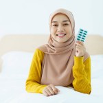 Asian young muslim woman showing a pill and water bottle, muslim woman taking a pill capsule. Health care and wellness in diverse ethnicity people and religious concept.