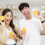 Happy cheerful Asian man and woman showing a half round of a fresh orange fruit to camera together and smiling.