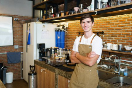 Photo for Professional young coffee barista standing inside the counter bar in the coffee shop and making arms crossed and looking at camera, handsome - good looking caucasian ethnic barista posing. - Royalty Free Image