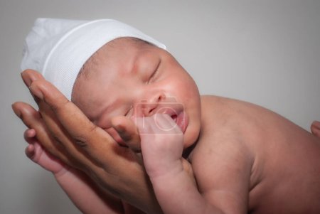 Foto de Bebé afroamericano sosteniendo su mano sobre un fondo negro con una manta blanca. - Imagen libre de derechos