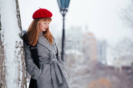 Photo for Young redhead woman in red winter hat walking snowy park - Royalty Free Image