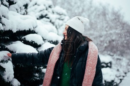 Photo for Young brunette woman in white winter hat walking snowy park - Royalty Free Image