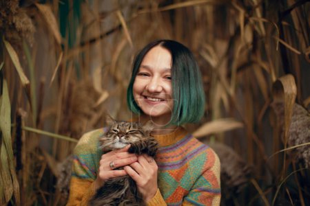 Photo for Young woman hugging cat, surrounded by dry plants - Royalty Free Image