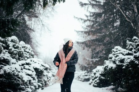 Téléchargez les photos : Jeune femme brune en chapeau blanc d'hiver marchant parc enneigé - en image libre de droit