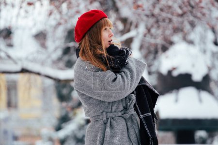 Téléchargez les photos : Jeune rousse femme en rouge chapeau d'hiver marche parc enneigé - en image libre de droit