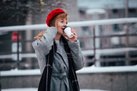 Young redhead woman in red winter hat walking snowy park 