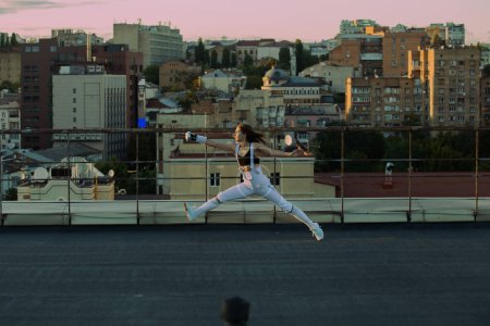Téléchargez les photos : Escrime femme pratique sur un toit avec la ville en arrière-plan - en image libre de droit