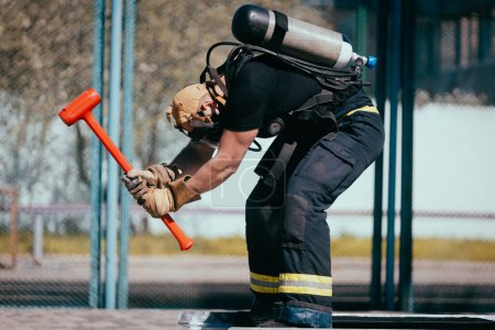 Photo for Male Firefighter with  oxygen balloon and hammer training on the sports ground. - Royalty Free Image