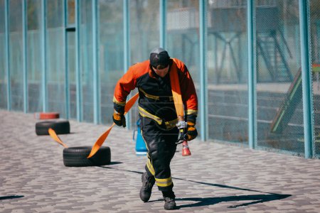 Téléchargez les photos : Pompier mâle avec tuyau d'entraînement sur le terrain de sport. - en image libre de droit