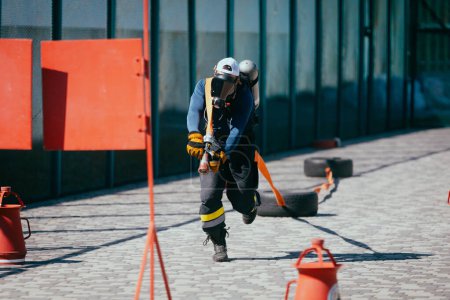 Téléchargez les photos : Pompier en cours d'exécution avec tuyau d'entraînement sur le terrain de sport. - en image libre de droit