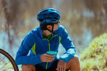Photo for Young man cyclist   enjoying his morning time in nature and drinking tea - Royalty Free Image