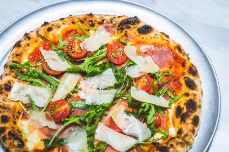 Photo for Neapolitan style pizza with cheese, patma ham, arugula, tomato sauce and cherry tomatoes - Royalty Free Image