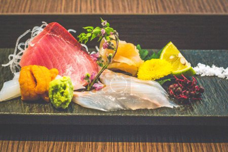 Photo for A dish of sashimi raw fish including tuna, squid, uni, sea urchin, wasabi and edible flowers - Royalty Free Image