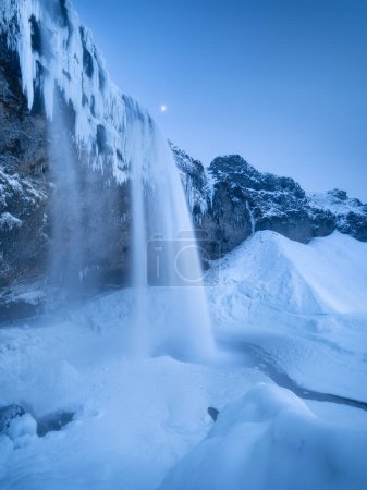 Téléchargez les photos : Cascade Seljalandsfoss, Islande. Paysage hivernal islandais. Haute cascade et rochers. Neige et glace. Puissant ruisseau d'eau de la falaise. Un endroit populaire pour voyager en Islande. - en image libre de droit