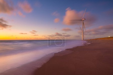 Photo for The surf on the seashore during sunset. Renewable energy sources. Wind turbines on the shore. Netherlands. A seascape during sunset. Bright sky during sunset. A sandy beach at low tide. Industria image. - Royalty Free Image