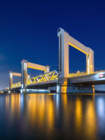 Photo for Botlek bridge, Rotterdam, Netherlands. View of the bridge at night.  Road for cars and railroad transport. Architectural landscape. Reflections on the surface of the water. - Royalty Free Image