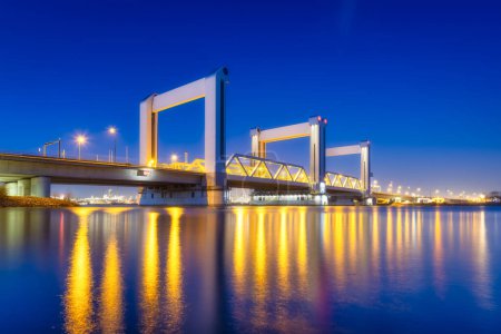 Foto de Botlek bridge, Rotterdam, Países Bajos. Vista del puente por la noche. Carretera para el transporte de automóviles y ferrocarril. Paraje arquitectónico. Reflexiones sobre la superficie del agua. - Imagen libre de derechos
