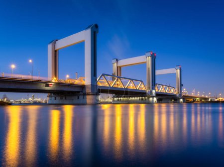 Photo for Botlek bridge, Rotterdam, Netherlands. View of the bridge at night.  Road for cars and railroad transport. Architectural landscape. Reflections on the surface of the water. - Royalty Free Image