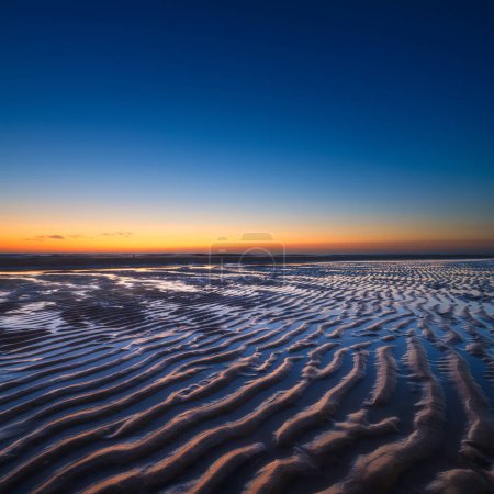 Téléchargez les photos : Un paysage marin au coucher du soleil. Des lignes de sable sur le rivage. Ciel lumineux au coucher du soleil. Une plage de sable à marée basse. Fond d'écran et fond. - en image libre de droit