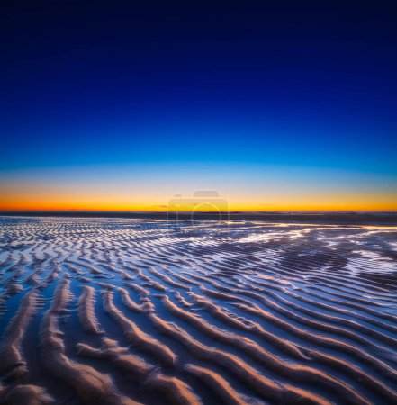 Foto de Un paisaje marino al atardecer. Líneas de arena en la orilla del mar. Cielo brillante durante la puesta del sol. Una playa de arena en marea baja. Fondo de pantalla y fondo. - Imagen libre de derechos