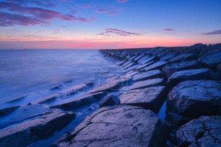 Photo for A seascape during sunset. The stone causeway during sunset. Sharp rocks. Bright sky during sunset. Long exposure. Photo for wallpaper. - Royalty Free Image