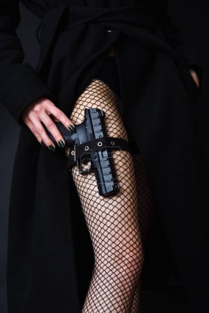 Dangerous young woman holding weapon. Femme fatale with gun and fish net stockings.