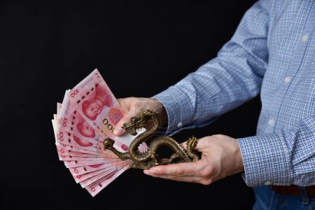 Geschäftsmann mit Geldscheinen in der Hand. Chinesisches RMB-Bargeld und symbolischer Drache.