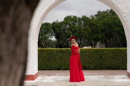 Foto de Esencia inspirada en Frida: Una mujer mexicana, que recuerda a Frida Kahlo, adorna una silla envejecida debajo de arcos delicados. Bañada en un juego de luz y sombra, su atuendo tradicional y su mirada contemplativa - Imagen libre de derechos