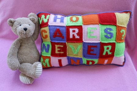 Téléchargez les photos : Ours en peluche assis à côté oreiller tricoté à la main avec des phrases négligentes multicolores - en image libre de droit