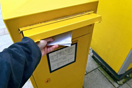 Foto de Persona irreconocible poniendo un sobre en la ranura de correo de un buzón amarillo. - Imagen libre de derechos