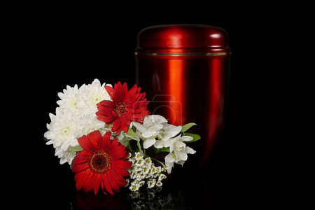 Photo for Funeral mourning urn next to a flower bouquet. Isolated on black background. - Royalty Free Image