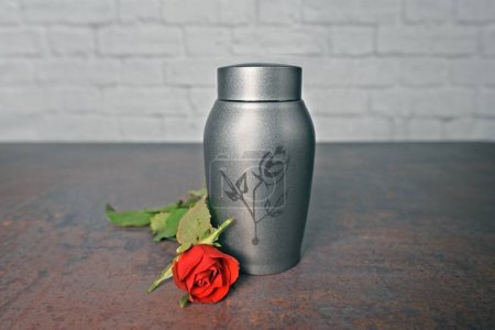 Photo for Funeral urn beside a red rose. Horizontal image with selective focus. - Royalty Free Image