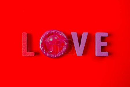 Foto de Letras de amor con condón sobre fondo rojo. Concepto educativo de sexo seguro y prevención de ETS. - Imagen libre de derechos