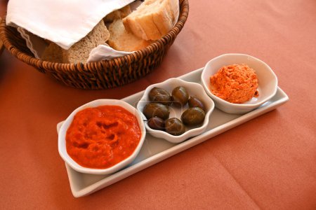 Téléchargez les photos : Entrées balkaniques : olives, sauce tomate et trempette au poivron rouge rôti servie avec du pain - en image libre de droit