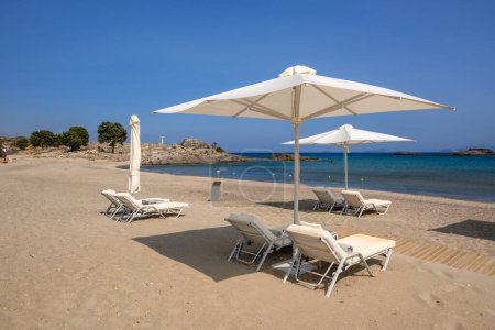 Sonnenliegen mit Sonnenschirm am Sandstrand von Agios Stefanos. Die griechische Insel Kos