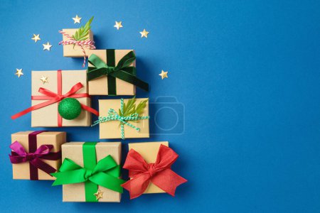 Christmas gift boxes with colorful ribbons on blue background in shape of Christmas tree. Holiday wrapping and packaging concept. Top above. Flat lay