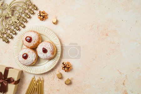 Jewish holiday Hanukkah concept with traditional donuts, menorah and gift box on stone background. Top view, flat lay