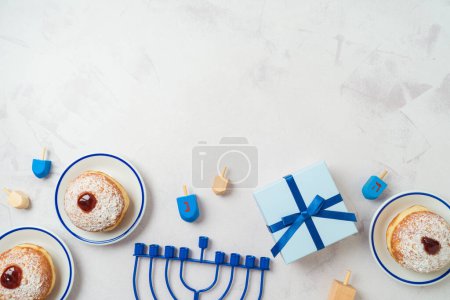 Hintergrund mit traditionellen süßen Donuts, Menora und Geschenkbox. Chanukka-Feiertag. Draufsicht, flache Lage
