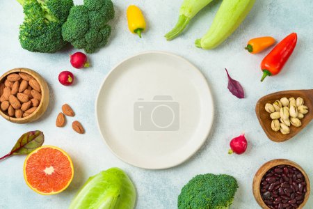 Foto de Vegetarian and vegan healthy lifestyle concept. Raw vegetables and fruits with empty plate over rustic background. Top view, flat lay - Imagen libre de derechos