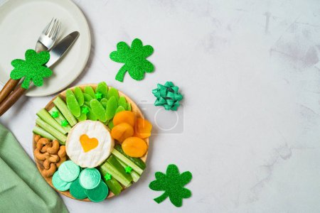 Foto de St Patricks day charcuterie board with cheese, dried fruits and  party decorations on bright background. Top view, flat lay - Imagen libre de derechos
