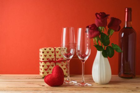 Photo for Valentine's day background. Wooden table with glasses, wine bottle and rose flowers over red background - Royalty Free Image