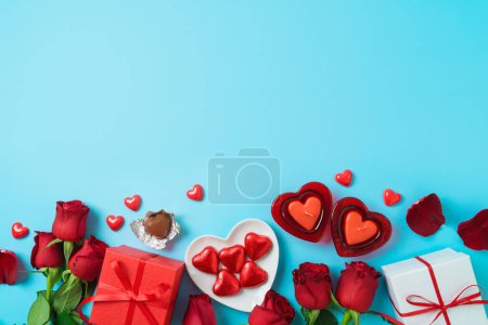 Foto de Valentines day celebration concept with heart shape chocolate, gift box and  rose flowers on blue background. Top view. Flat lay - Imagen libre de derechos
