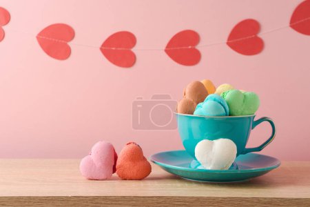 Photo for Heart shape macaroons french cookies in coffee cup with heart shape garland over pink background. Valentines day greeting card - Royalty Free Image