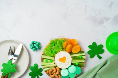 Foto de St Patrick's day charcuterie board with cheese, dried fruits and  party decorations on bright background. Top view, flat lay - Imagen libre de derechos
