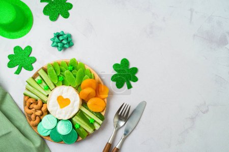 Foto de St Patricks day table setting with charcuterie board, cheese, dried fruits and  shamrock on stone background. Top view, flat lay - Imagen libre de derechos